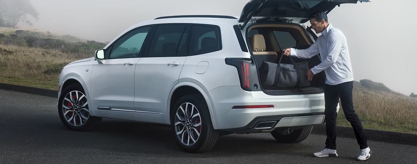 A man loading cargo into the back of a white 2024 Cadillac XT6.