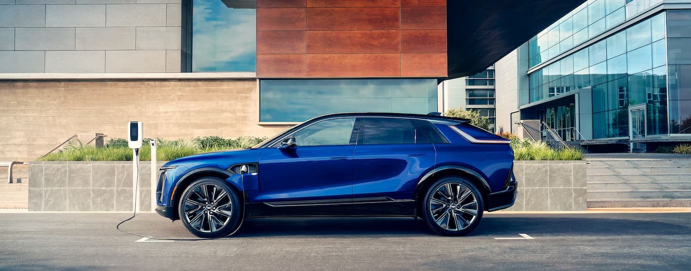 A blue 2024 Cadillac LYRIQ is parked on the side of a street charging.