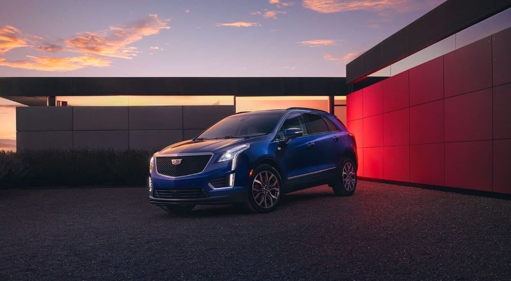 A close up shows a blue 2024 Cadillac XT5 for sale parked on a gravel driveway.