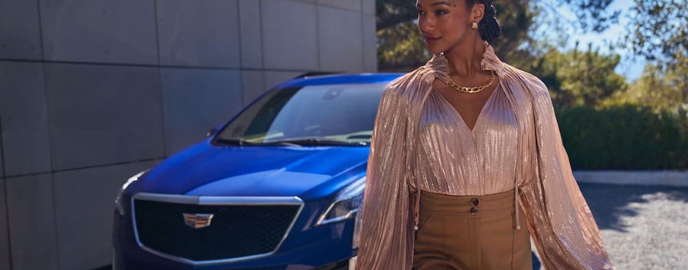 A smiling person is shown walking past a blue 2024 Cadillac XT5.