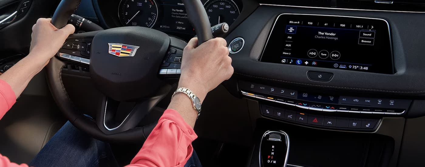 A close up of a person holding the steering wheel in a 2023 Cadillac XT4 is shown.