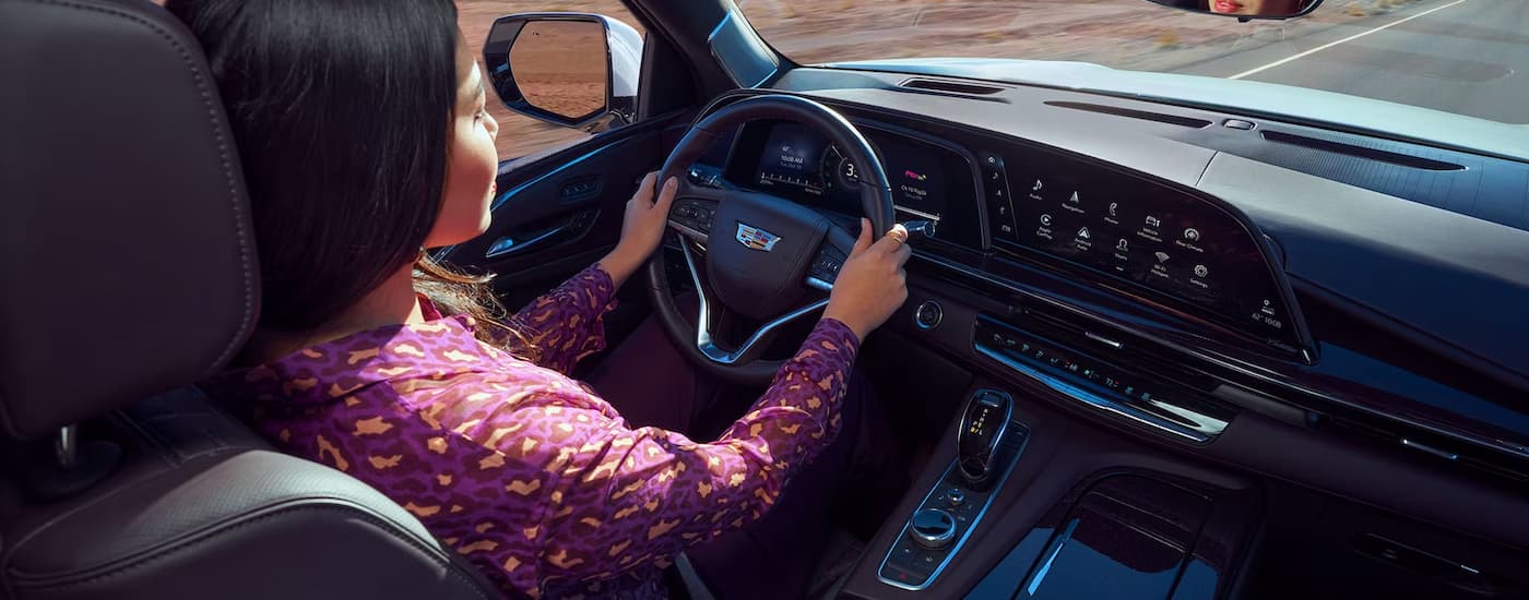 A woman is shown driving a 2023 Cadillac Escalade on an open road.