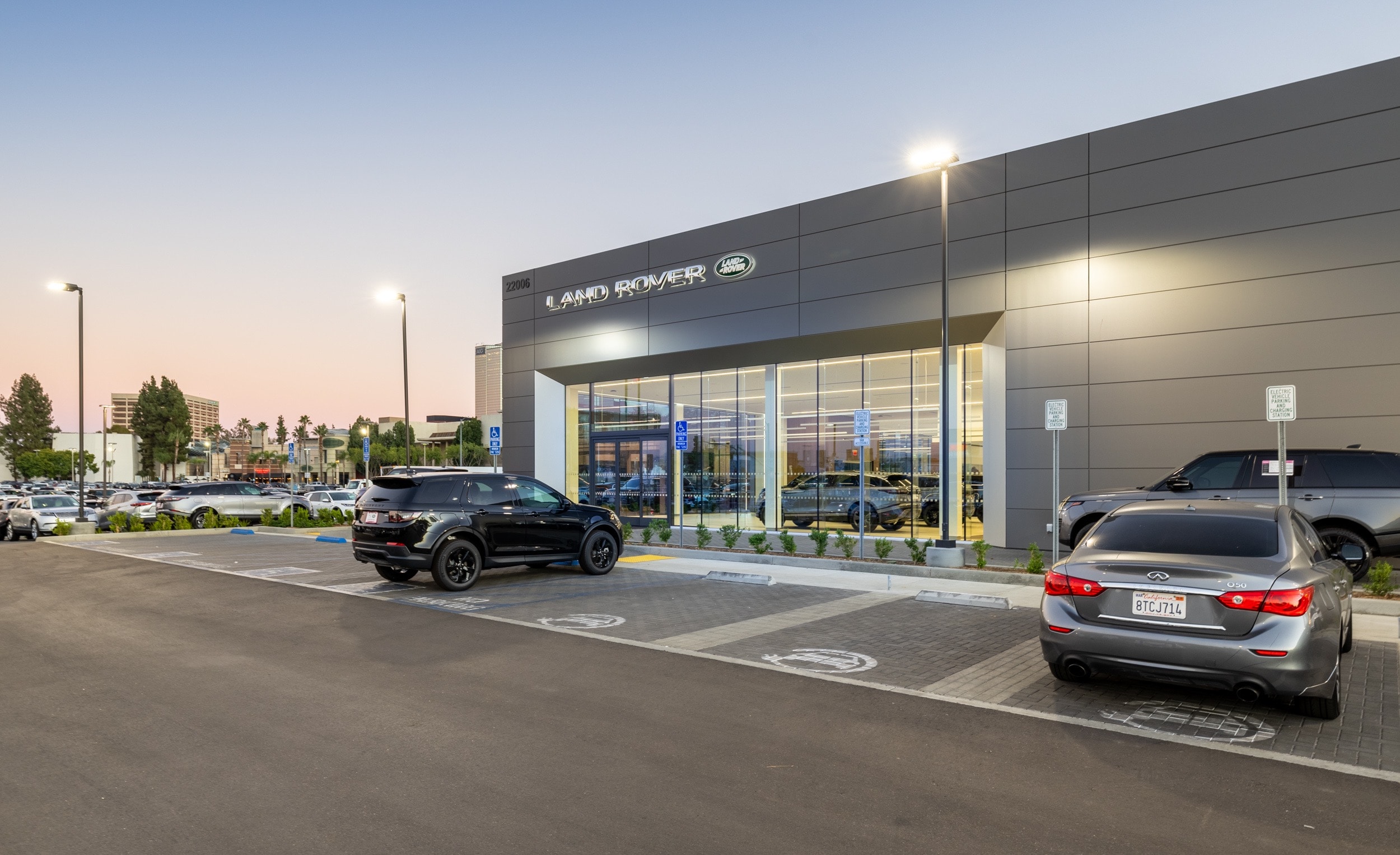 Front view of Land Rover Woodland Hills building with large windows in the front. The sky is clear, and it appears to be evening as parking lot lights are on.