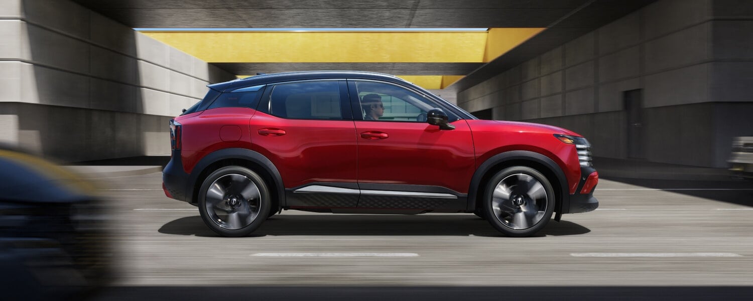 A side view of a red 2025 Nissan Kicks SR driving on a highway.