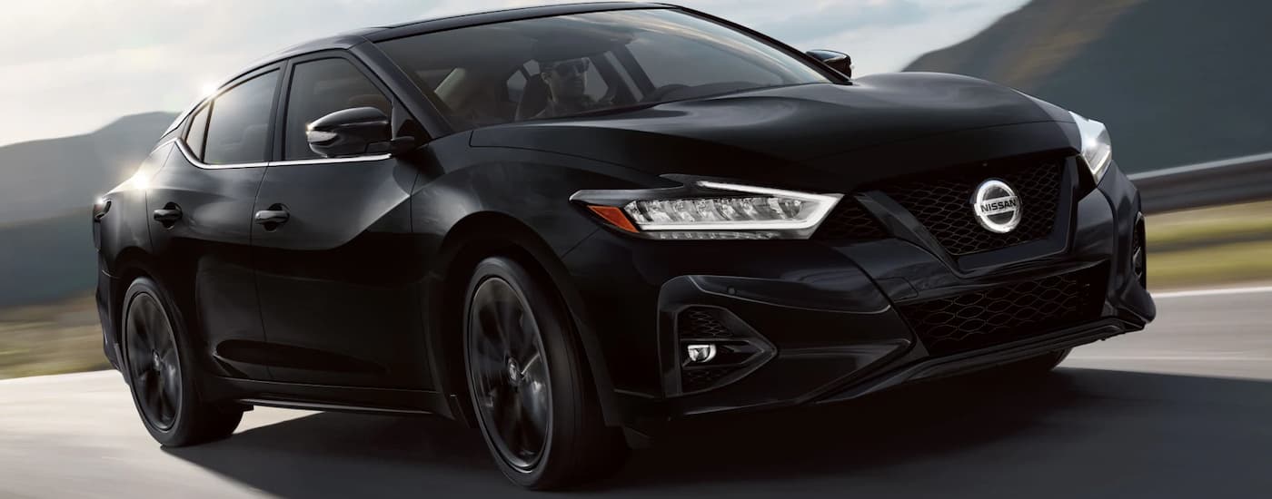 A black 2022 Nissan Maxima is driving on an open road after viewing a used Nissan for sale at a dealer.