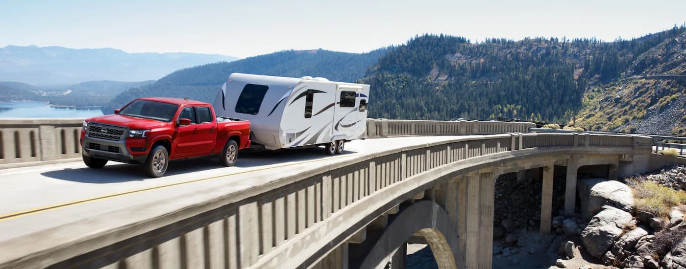 Red 2026 Nissan Frontier towing a trailer on a winding highway