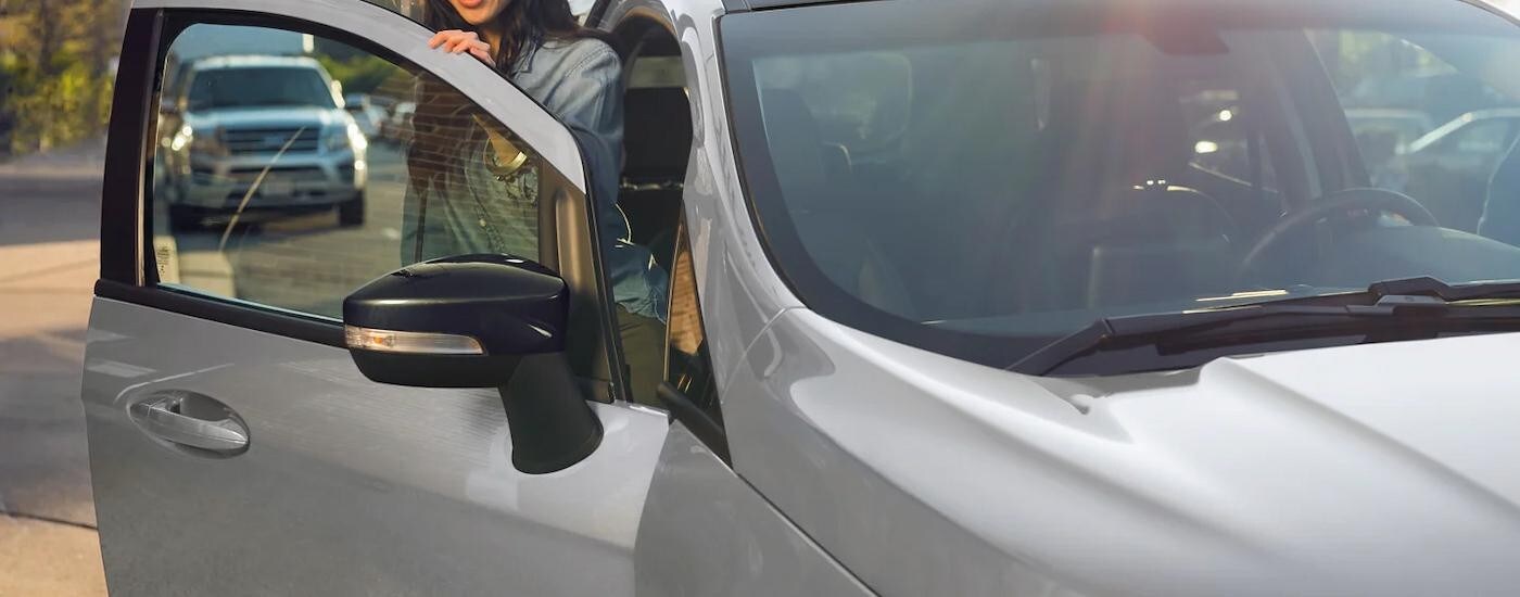 A person is getting out of a grey used vehicle at a used car dealer.