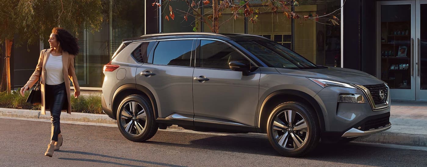 A woman is walking away from a grey 2022  Nissan Rogue parked on the side of a city street.