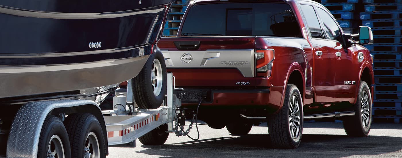 A rear view of a red 2022 Nissan Titan Platinum is towing a boat on a trailer.