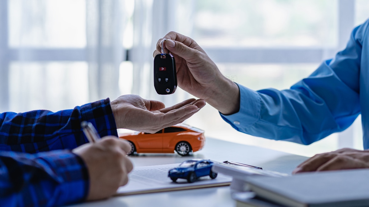 A salesperson giving a car key fob to someone signing a contract for their new car