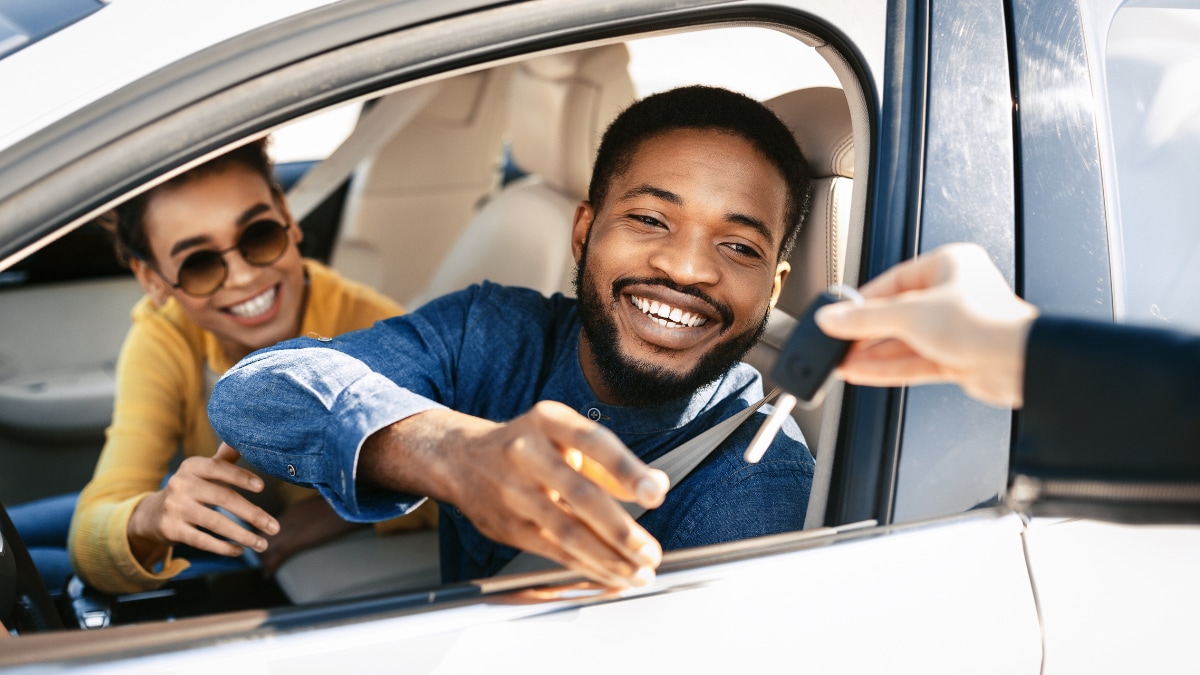 A couple receiving their car keys while inside the vehicle from a salesperson