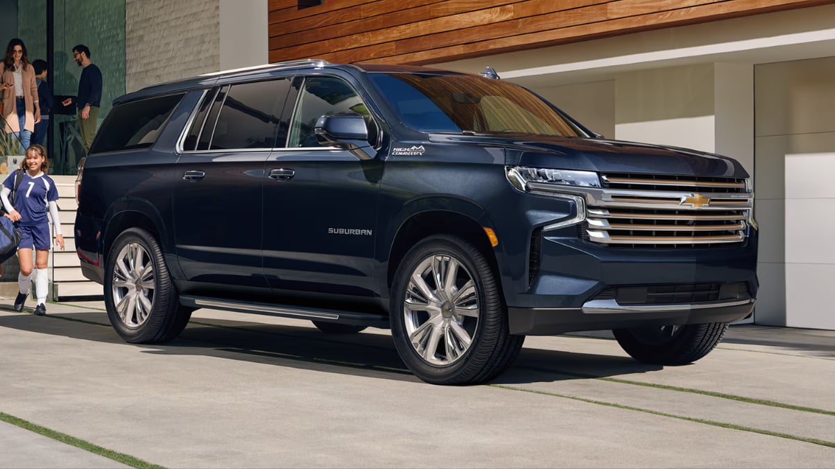 A black Chevrolet Suburban parked in a driveway with a family approaching it from their house