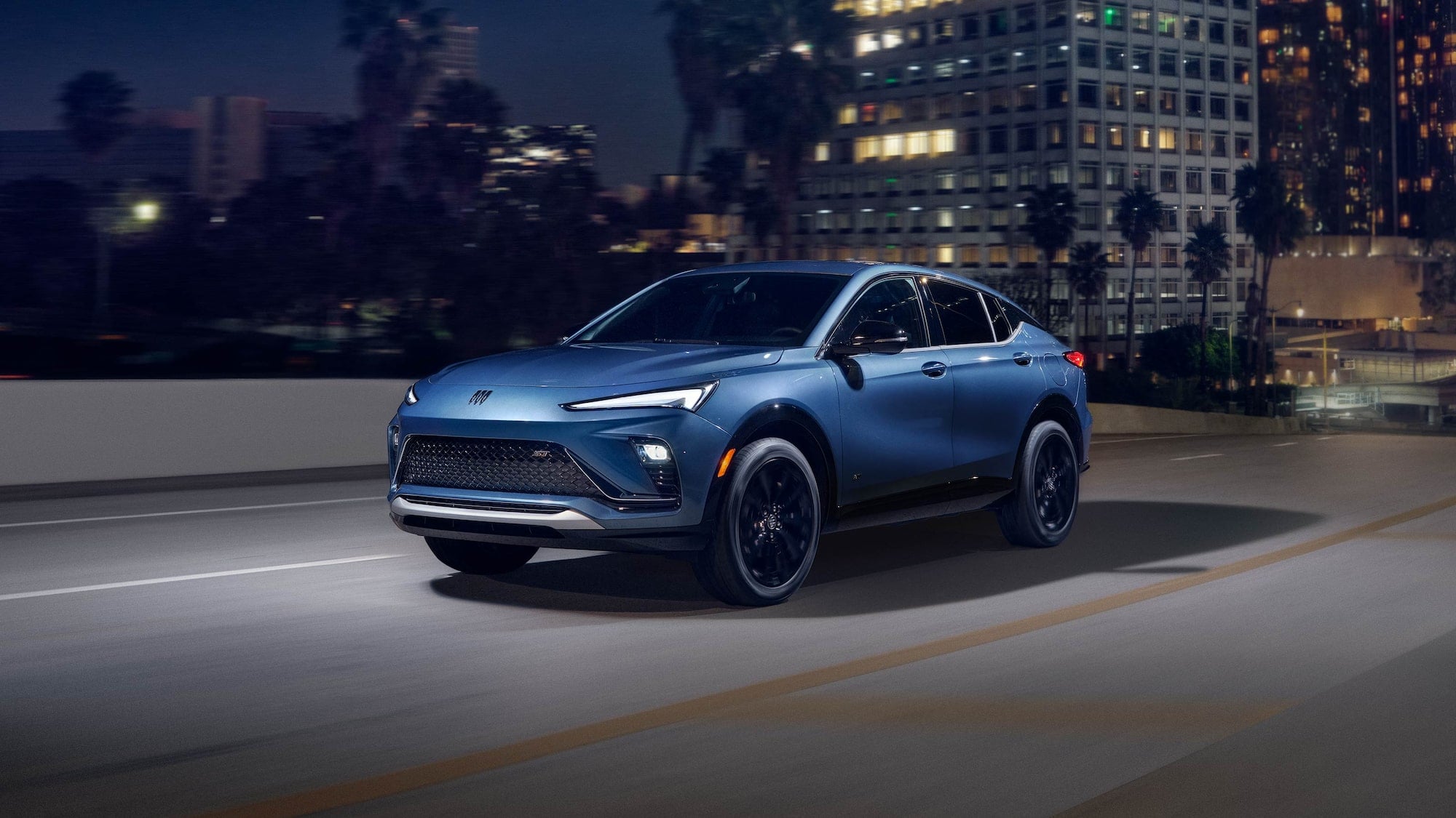 A blue Buick Envista driving around at night, leaving a city