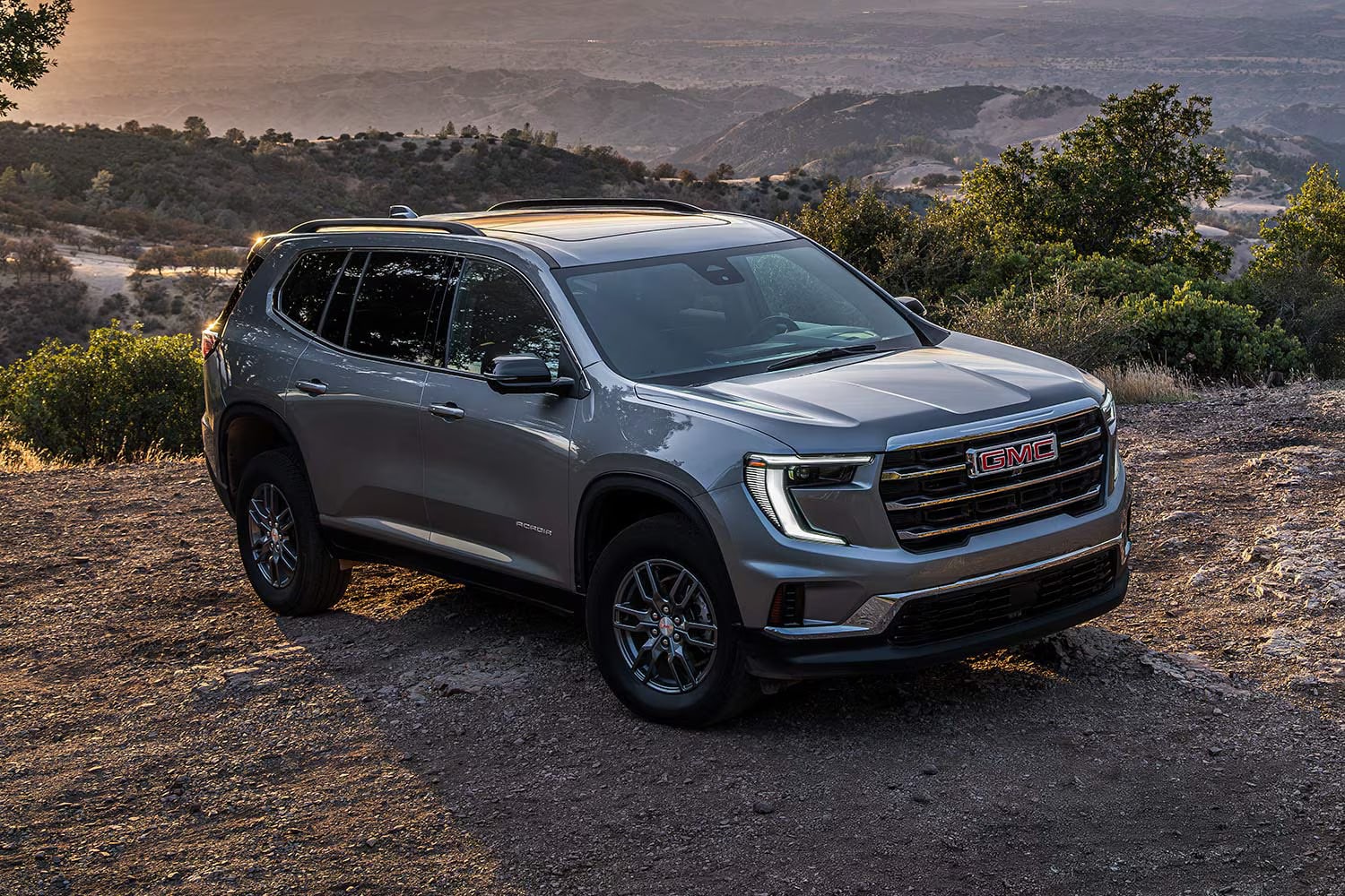 A gray GMC Acadia parked off-road over a hilly region