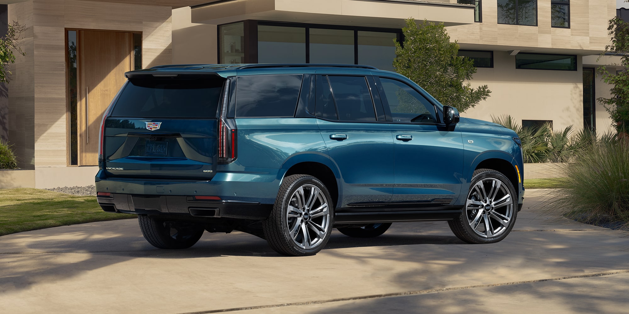 A side view of a light blue Cadillac Escalade parked in front of a nice house