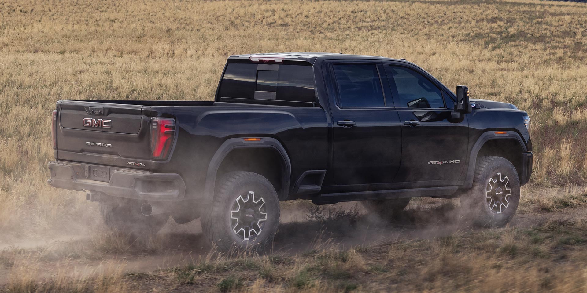 A dark blue GMC Sierra HD driving over a dirt road through a field