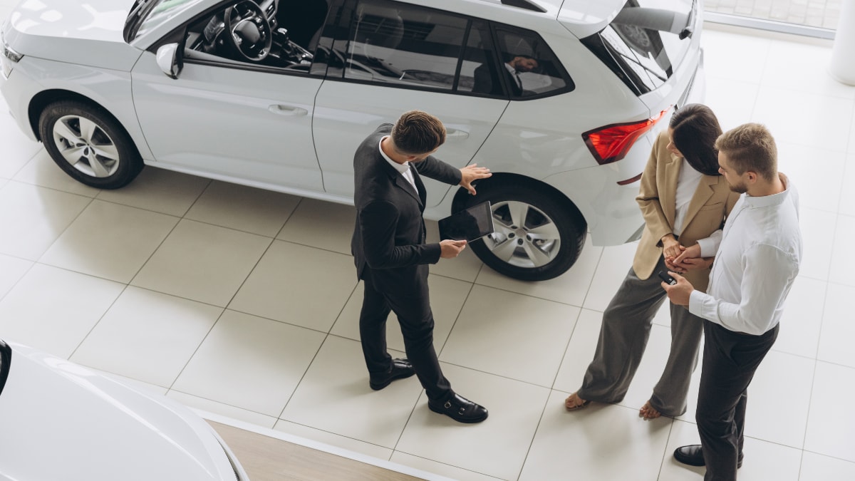 A car salesperson showing a white SUV off to a couple