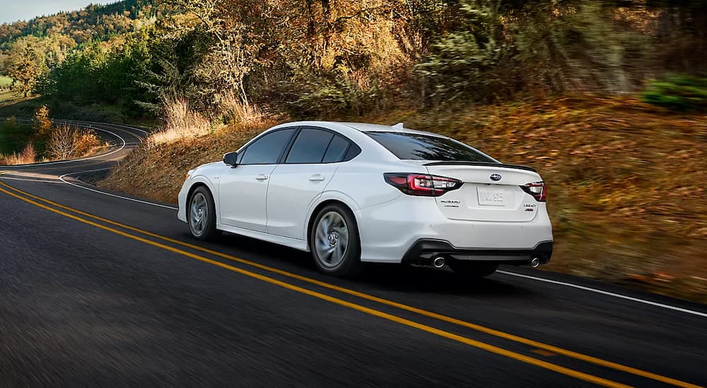 A white 2023 Subaru Legacy is shown driving on a winding road after leaving Albany Subaru Legacy dealer.