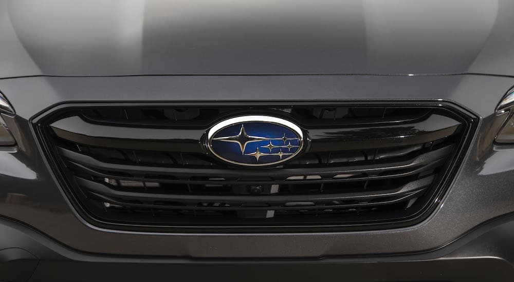 A close up shows the Subaru badge on the grille of a dark grey 2020 Subaru Outback.