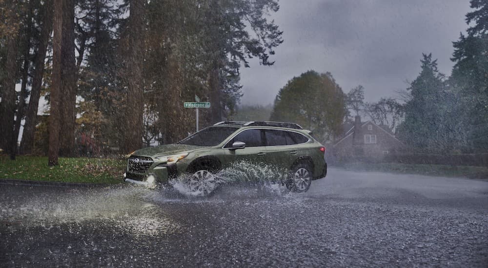 A green 2023 Subaru Outback is shown driving on a rainy day after leaving a Subaru Outback dealer.