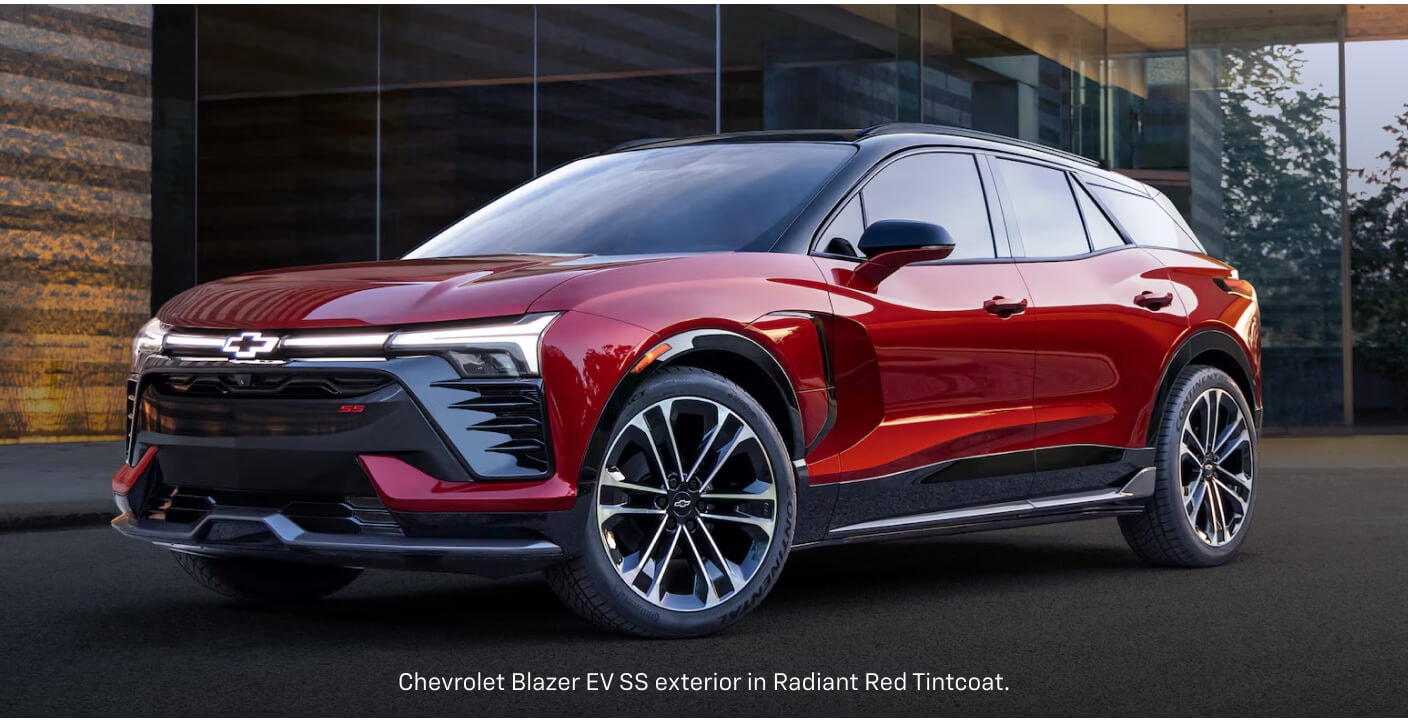 Front three-quarter view of a red Chevrolet Blazer EV SS parked in front of a modern glass building.