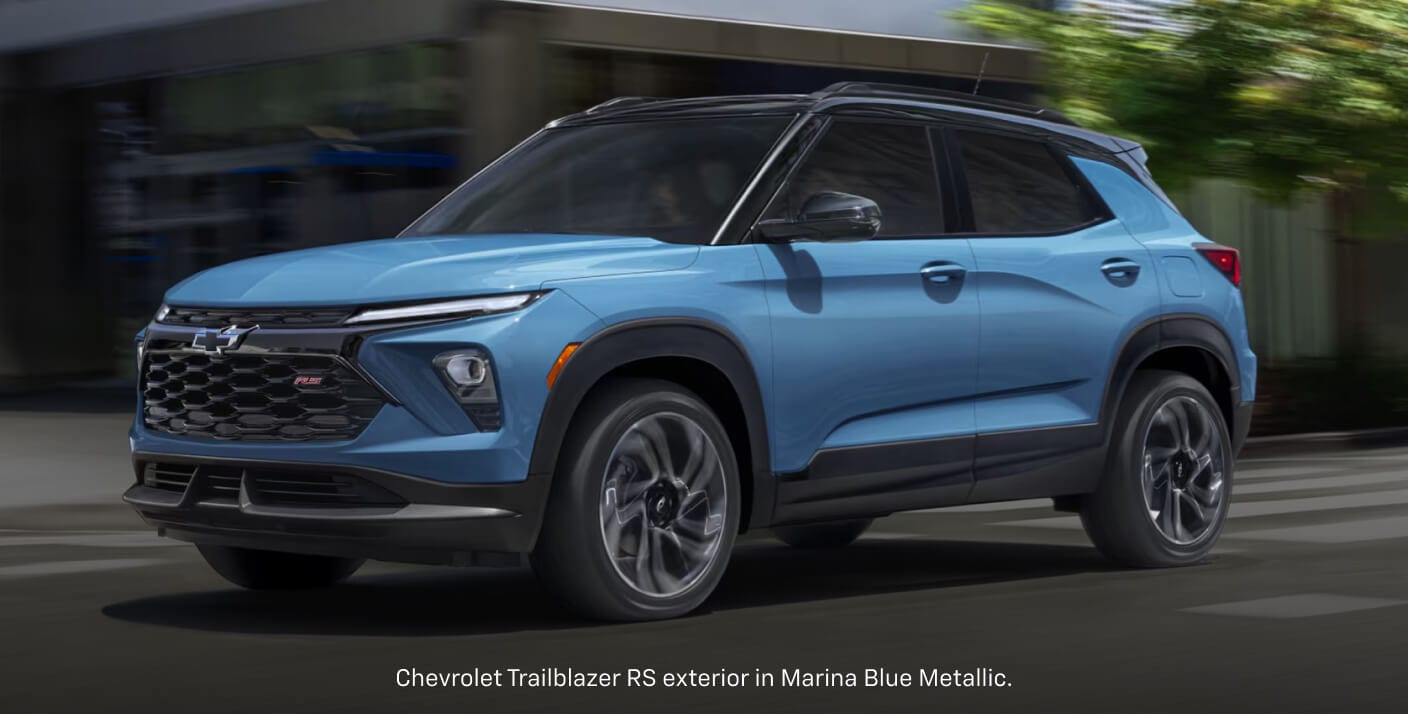 Front three-quarter view of a blue Chevrolet Trailblazer RS driving down a tree-lined city street.