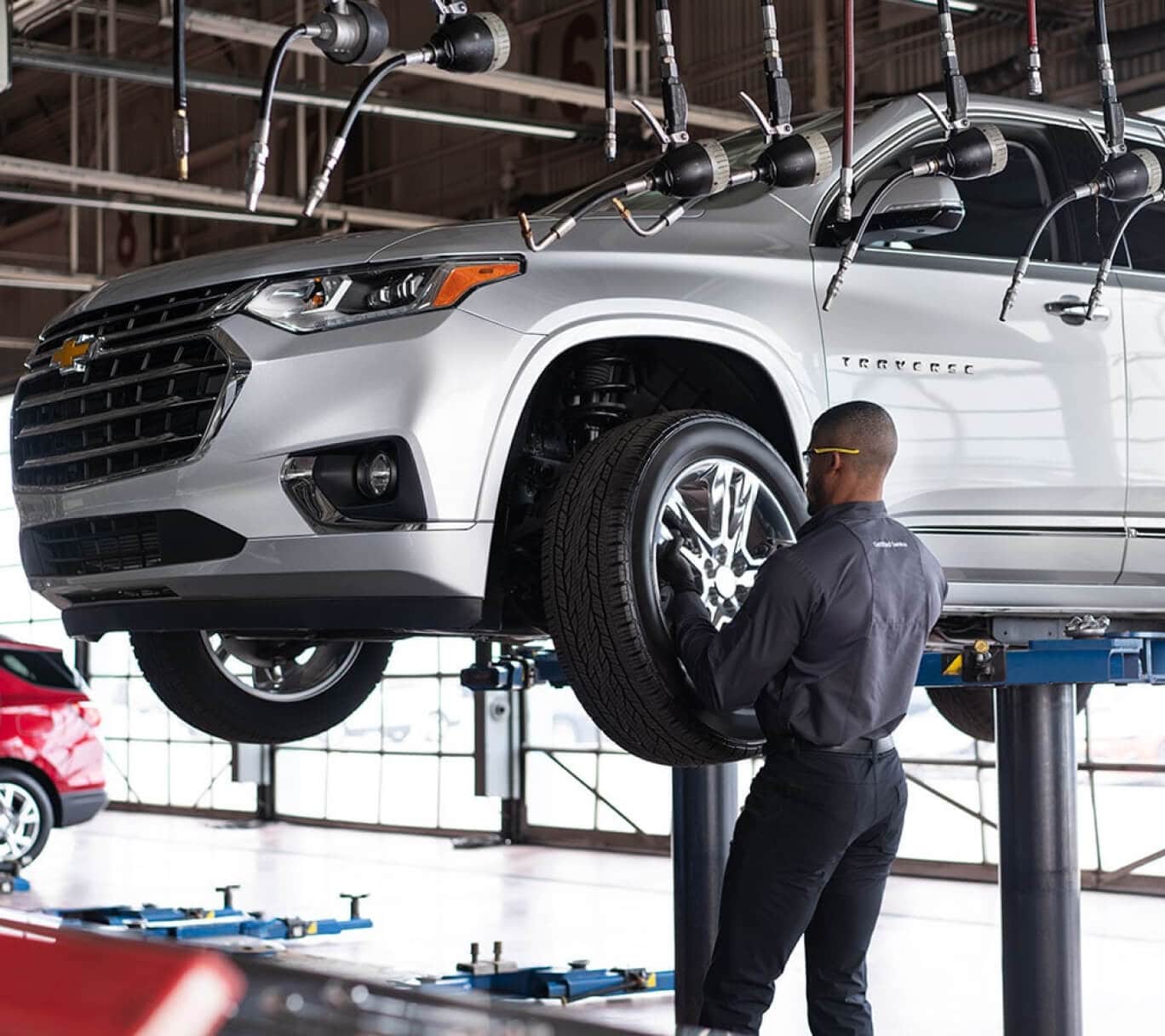A Chevrolet Certified Technician replaces a wheel on a lifted silver Chevy Traverse.