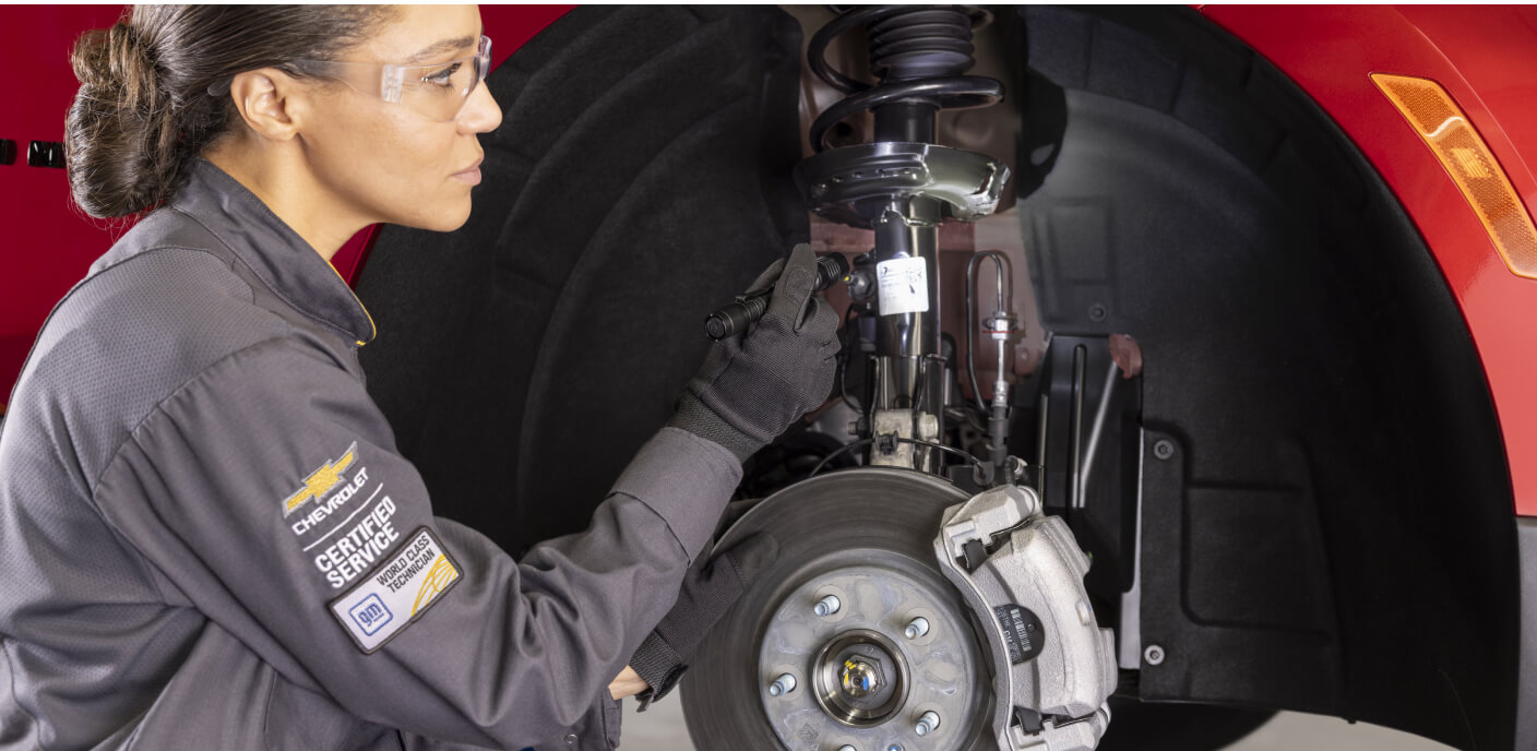 Side view of a Chevrolet Certified Service technician using a flashlight to inspect a vehicle's suspension.