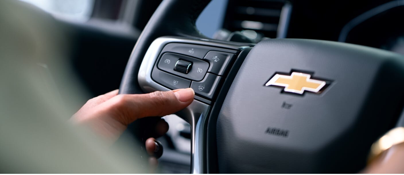 Close-up view of a driver's hand pressing a steering wheel button inside a Chevrolet Vehicle.