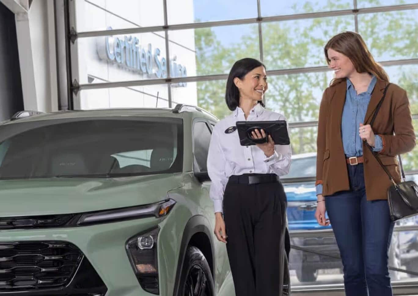 A Chevrolet Sales Associate assists a customer while walking near a green Chevy Trailblazer.