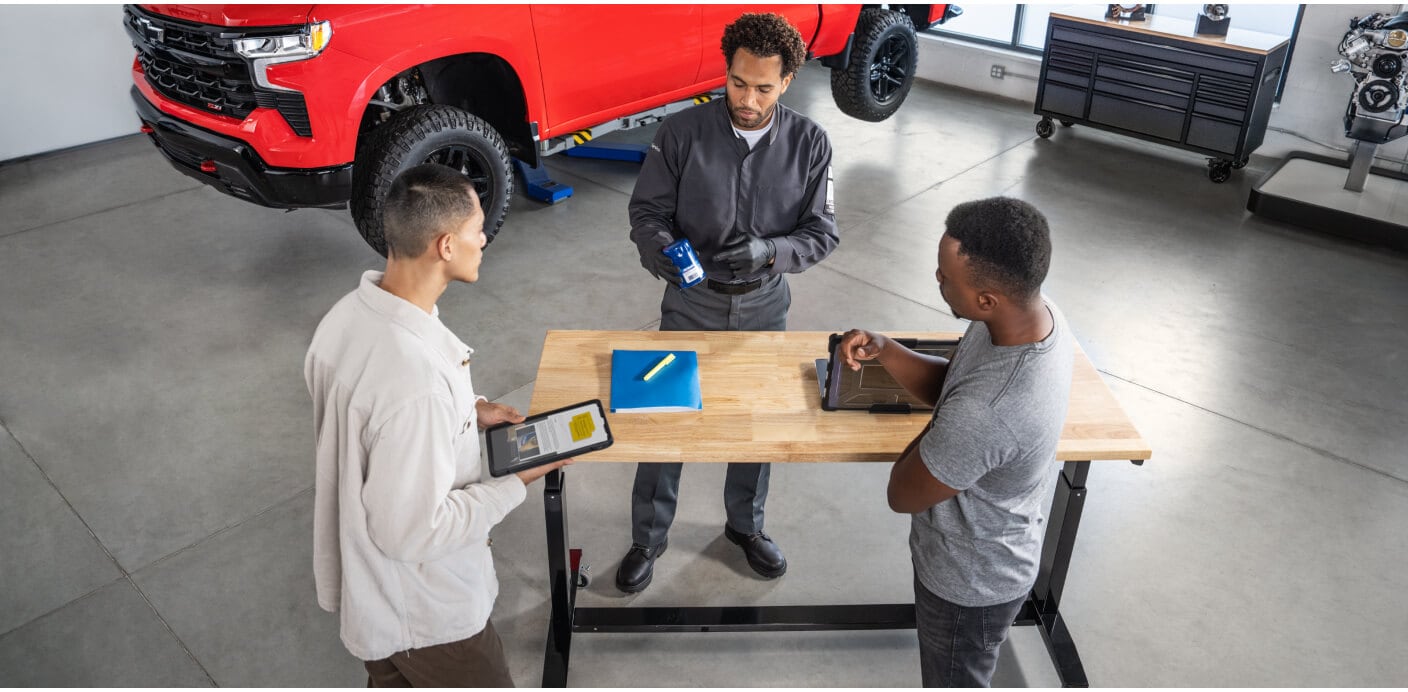 High-angle view of a service technician showing parst to customers at a workbench next to red Silverado ZR2.