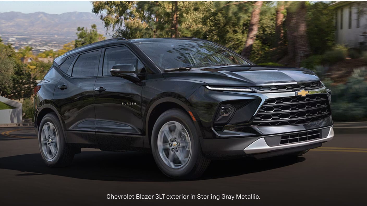 Front three-quarter view of a gray Chevrolet Blazer 3LT driving along a winding suburban road.