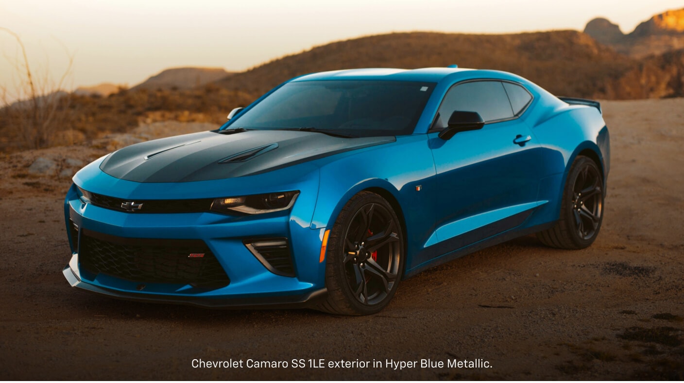 Front three-quarter view of a blue Chevrolet Camaro SS 1LE parked on a dirt path at sunset.