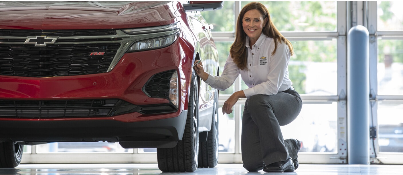 Low-angle view of a Chevrolet Certified Technician inspecting the tire of a red Equinox RS inside a dealership