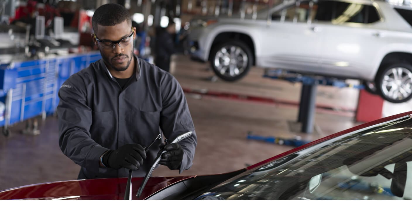 Medium shot of a Chevrolet technician in safety glasses replacing windshield wiper blades in a dealership.
