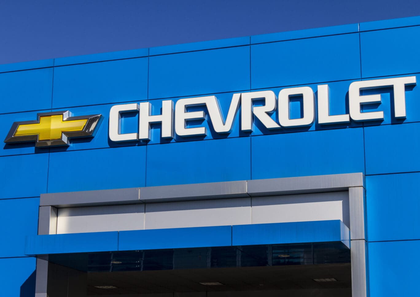 Low angle street perspective of a Chevrolet dealership sign in front of a clear blue sky.
