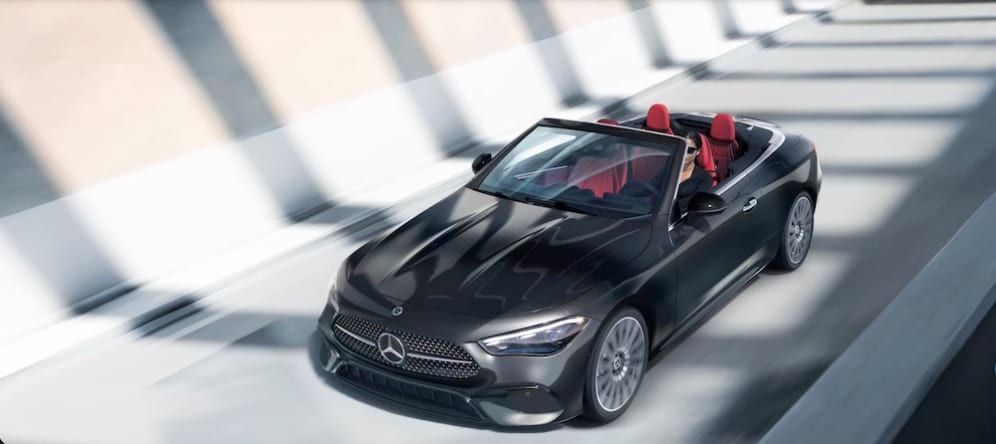 A woman driving a black Mercedes-Benz convertible down a highway