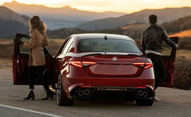 Couple getting out of red Alfa Romeo Giulia watching sunrise.