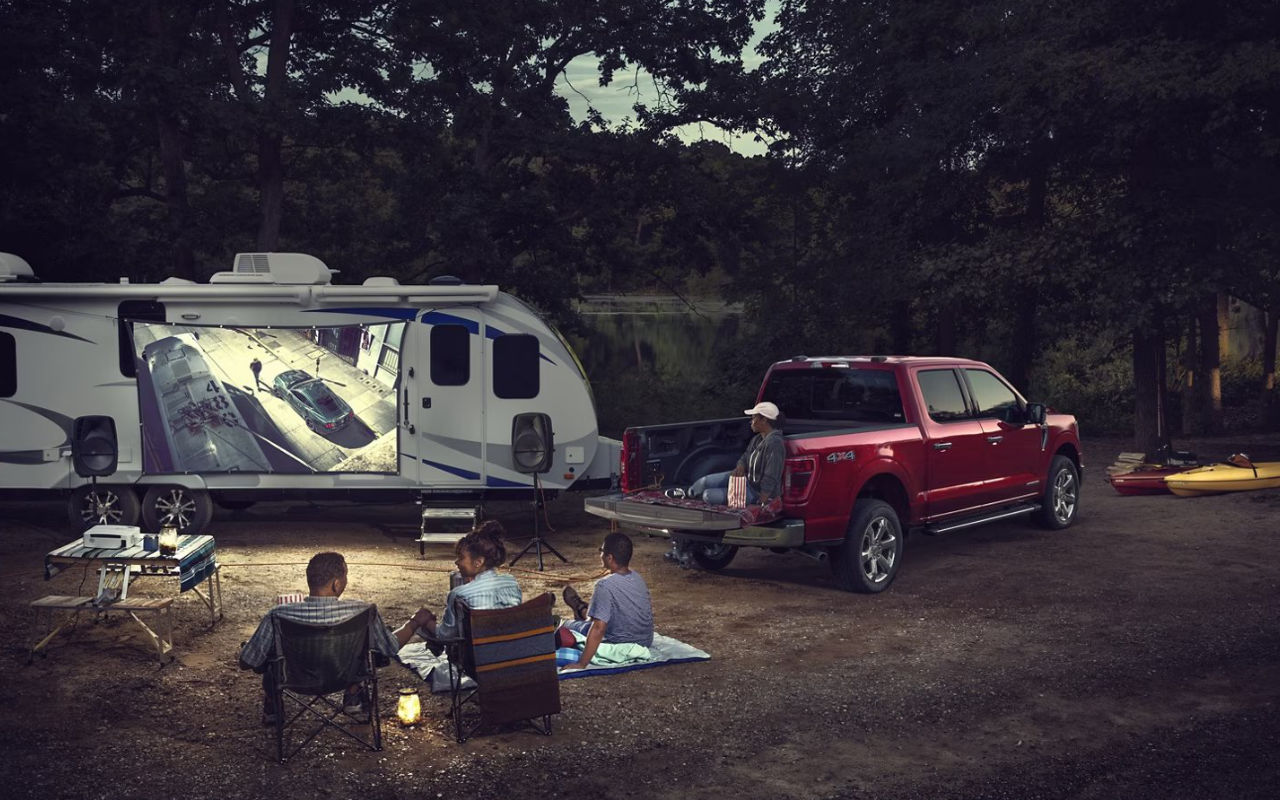 family of campers watching a movie projected on the side of a fifth wheel hithed to a Ford F-150 2023