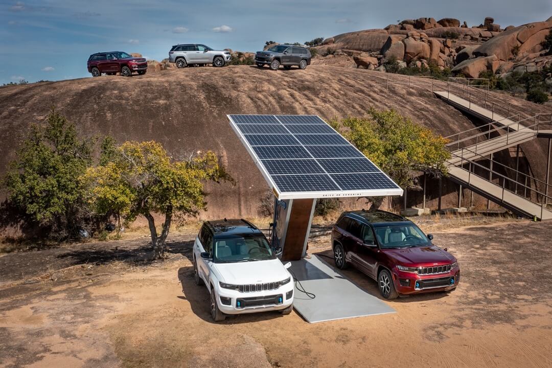 La gamme de différentes versions du Jeep Grand Cherokee 2023 à côté d'une station électrique.