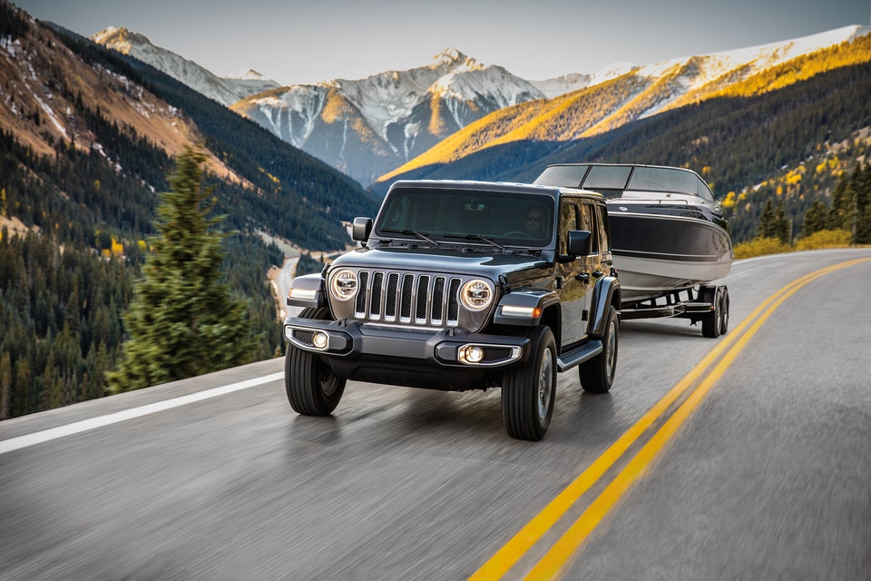 front side view of a 2023 Jeep Wrangler towing a boat on a country road