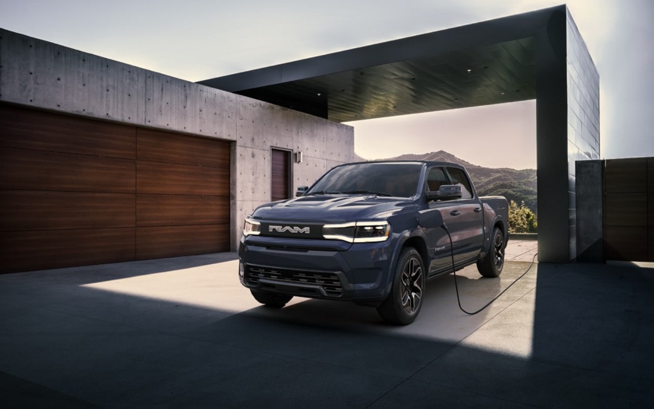 front side view of a RAM 1500 electric 2024 truck recharging next to a house