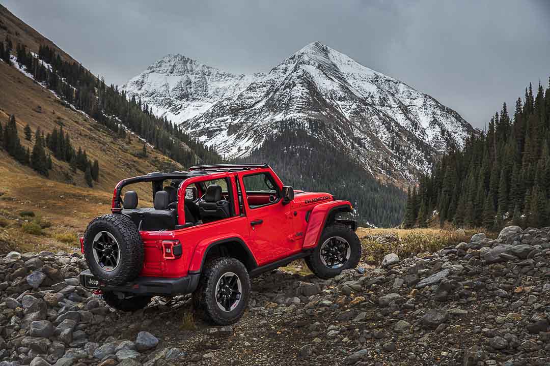 Vue 3/4 arrière d'un Jeep Wrangler Rubicon 2021 rouge garé sur des rochers et hors-route autour de rocheuses