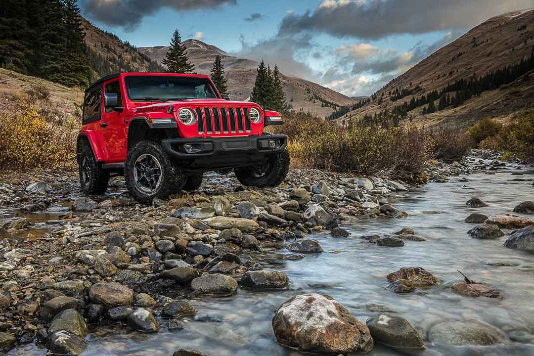 Vue 3/4 avant d'un Jeep Wrangler Rubicon 2021 rouge garé au bord d'un ruisseau en forêt