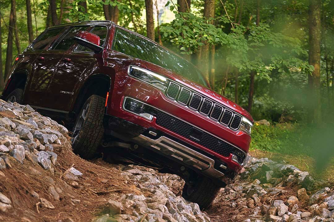 Un Jeep Wagoneer 2022 rouge parcourant des rochers hors-route dans une forêt