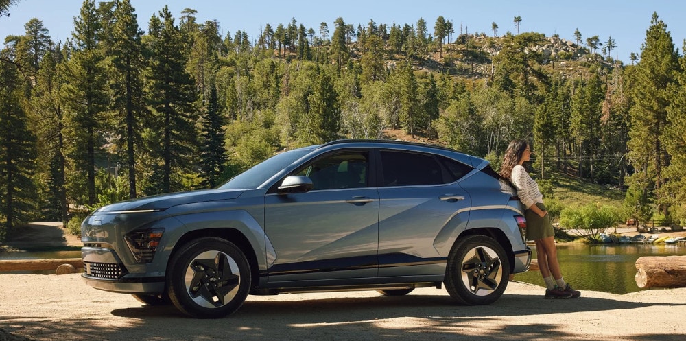 2024 Hyundai Kona in the woods with a woman leaning up against it