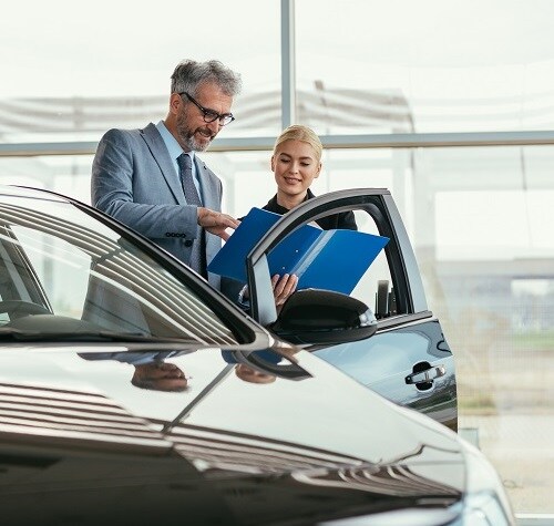 Sales agent showing a CPO car brochure to customer in car dealer's showroom