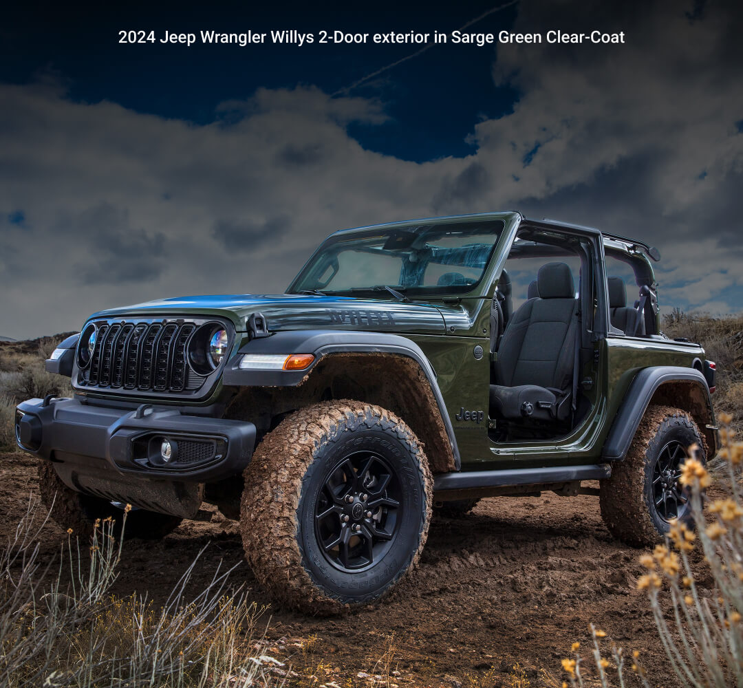 Front three-quarter view of 24 Jeep Wrangler Willys in Sarge Green navigating a muddy track in a rugged outdoor trail setting.