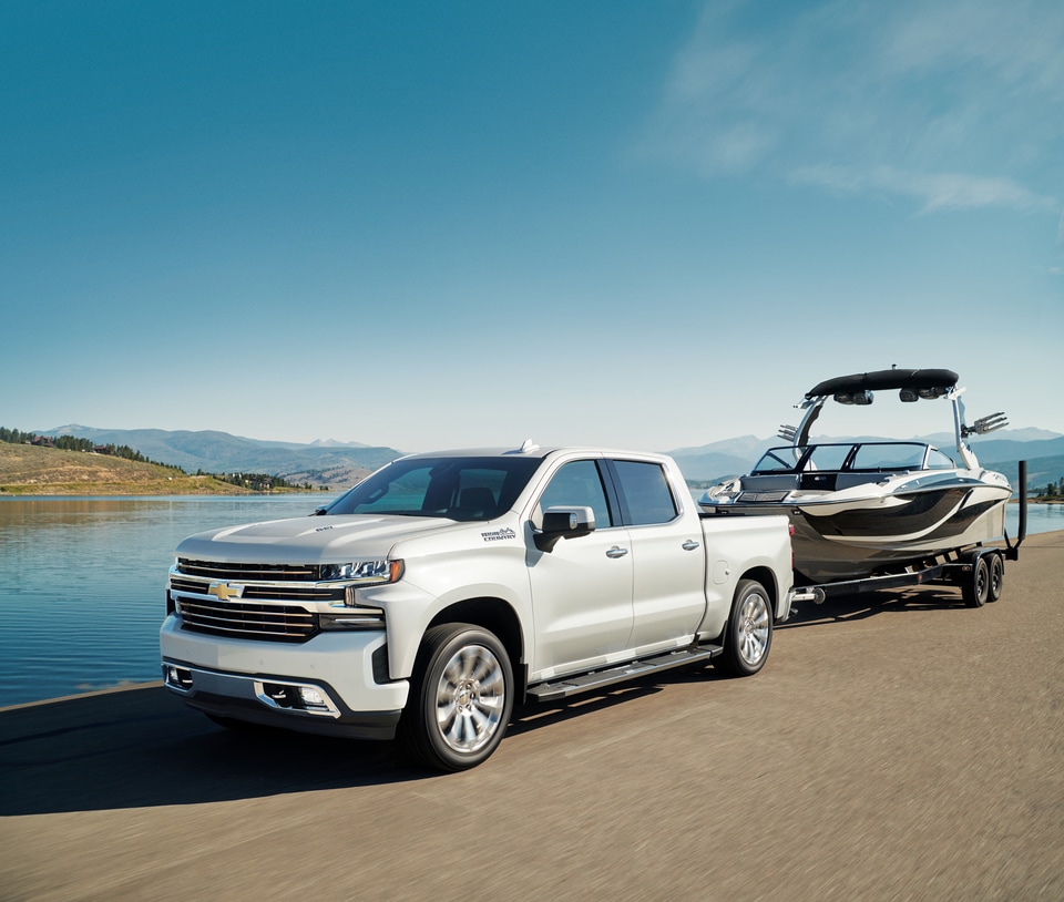 2025 Chevy Silverado High Country towing a boat by a lake.