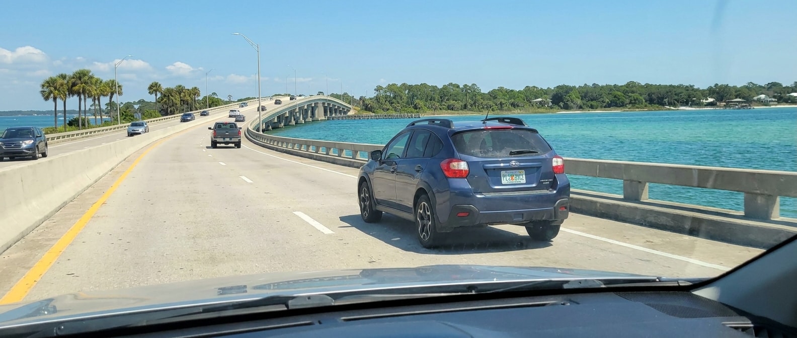 A used compact crossover or sedan driving across the Hathaway Bridge on US-98 on a bright 2026 Florida summer morning, St. Andrews Bay visible below, light traffic on the bridge approach